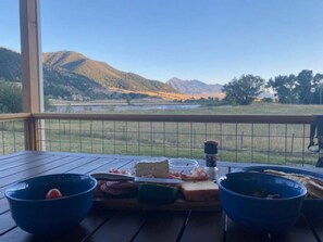 A table with food items on a balcony overlooking a mountainous landscape. - Evergreen Lane Getaway · River Views and Front Porch Sitting in Paradise (Livingston)