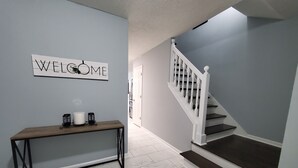 A hallway with a 'WELCOME' sign, a wooden bench, and a staircase with white railings. - Stone Mountain Escape 4 Bedroom Private Home (Stone Mountain)