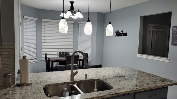 A kitchen with a granite countertop, stainless steel sink, and a dining area with a table and chairs. - Stone Mountain Escape 4 Bedroom Private Home (Stone Mountain)