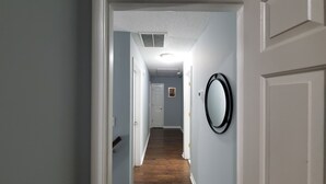 A hallway with a wooden floor, a white door on the right, and a wall-mounted mirror. - Stone Mountain Escape 4 Bedroom Private Home (Stone Mountain)