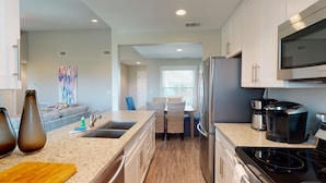 A modern kitchen with granite countertops, stainless steel appliances, and a dining area with a view. - Second Floor Condo With Bay View, Shared Pool, Pet Friendly (Port Aransas)