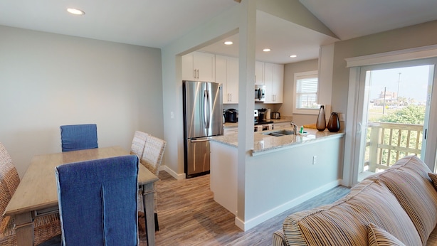 A modern kitchen with stainless steel appliances, a dining area with blue chairs, and a balcony with a view. - Second Floor Condo With Bay View, Shared Pool, Pet Friendly (Port Aransas)