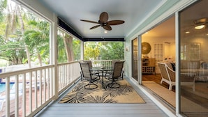 A covered patio with a table and chairs, a ceiling fan, and a view of a pool and greenery. - Fairway Villa w/ Private Pool  (Key West)
