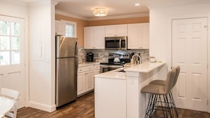 A modern kitchen with white cabinets, stainless steel appliances, and a central island with bar stools. - Fairway Villa w/ Private Pool  (Key West)