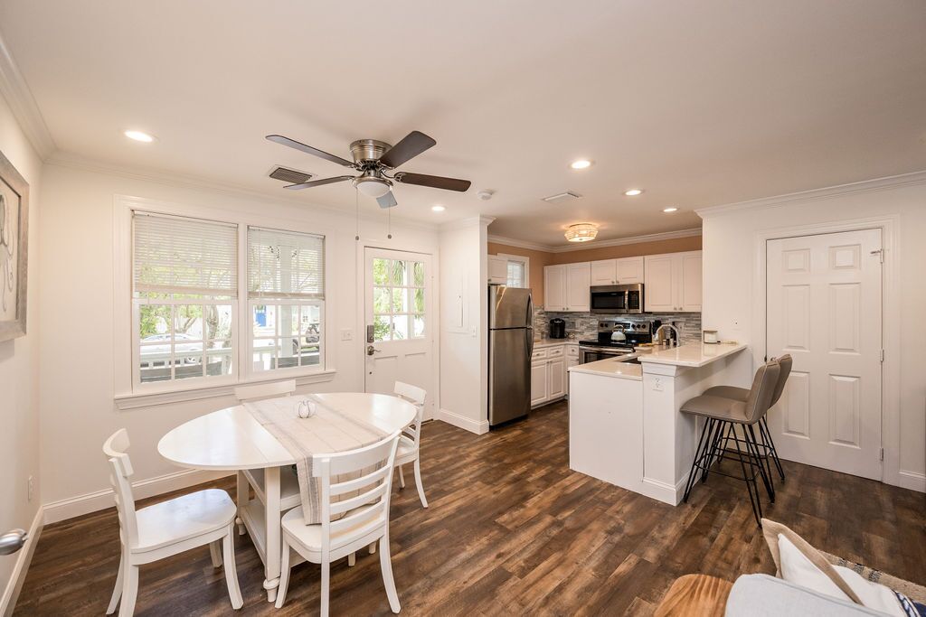 A modern kitchen with white cabinetry, a central island, and a dining area with white chairs.