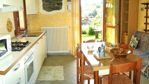 Une cuisine compacte avec un coin repas, un mur en pierre et une vue sur un jardin, accessible par une porte ouverte.