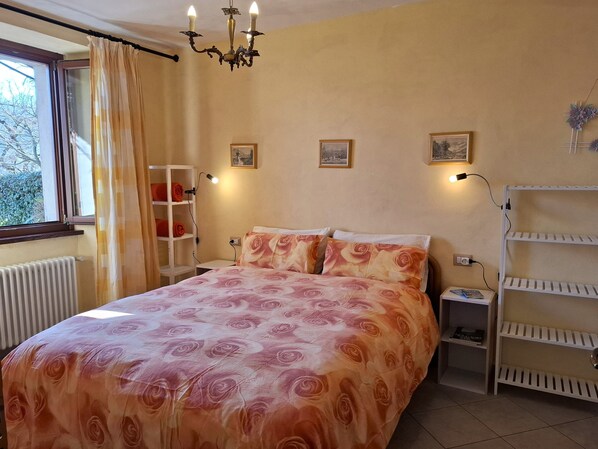 A bedroom with a bed, a nightstand, a shelf, and a radiator. - Apartment in an old barn, private garden overlooking the village (Plesio)