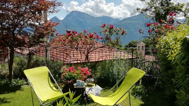 Un jardin avec deux chaises jaunes, une table avec un plateau et un parasol rouge.