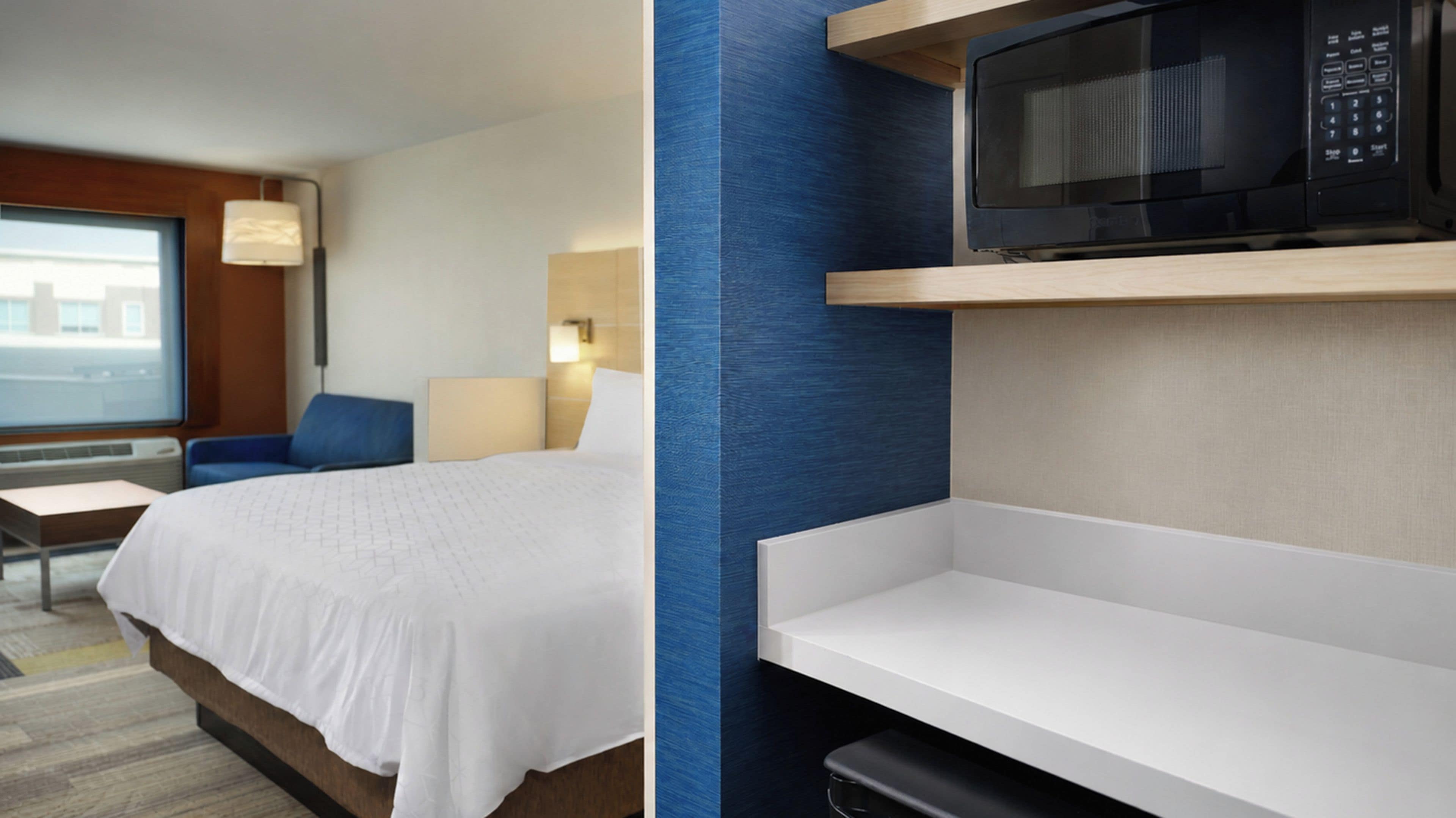 A hotel room with a bed, a desk, a chair, a microwave, and a window with a view.