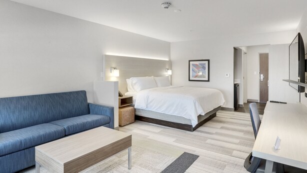 A modern hotel room with a bed, a blue sofa, a wooden coffee table, and a desk with a chair.