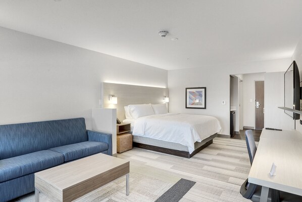 Et moderne hotelværelse med en seng, en blå sofa, et træbord og et skrivebord med stol.
