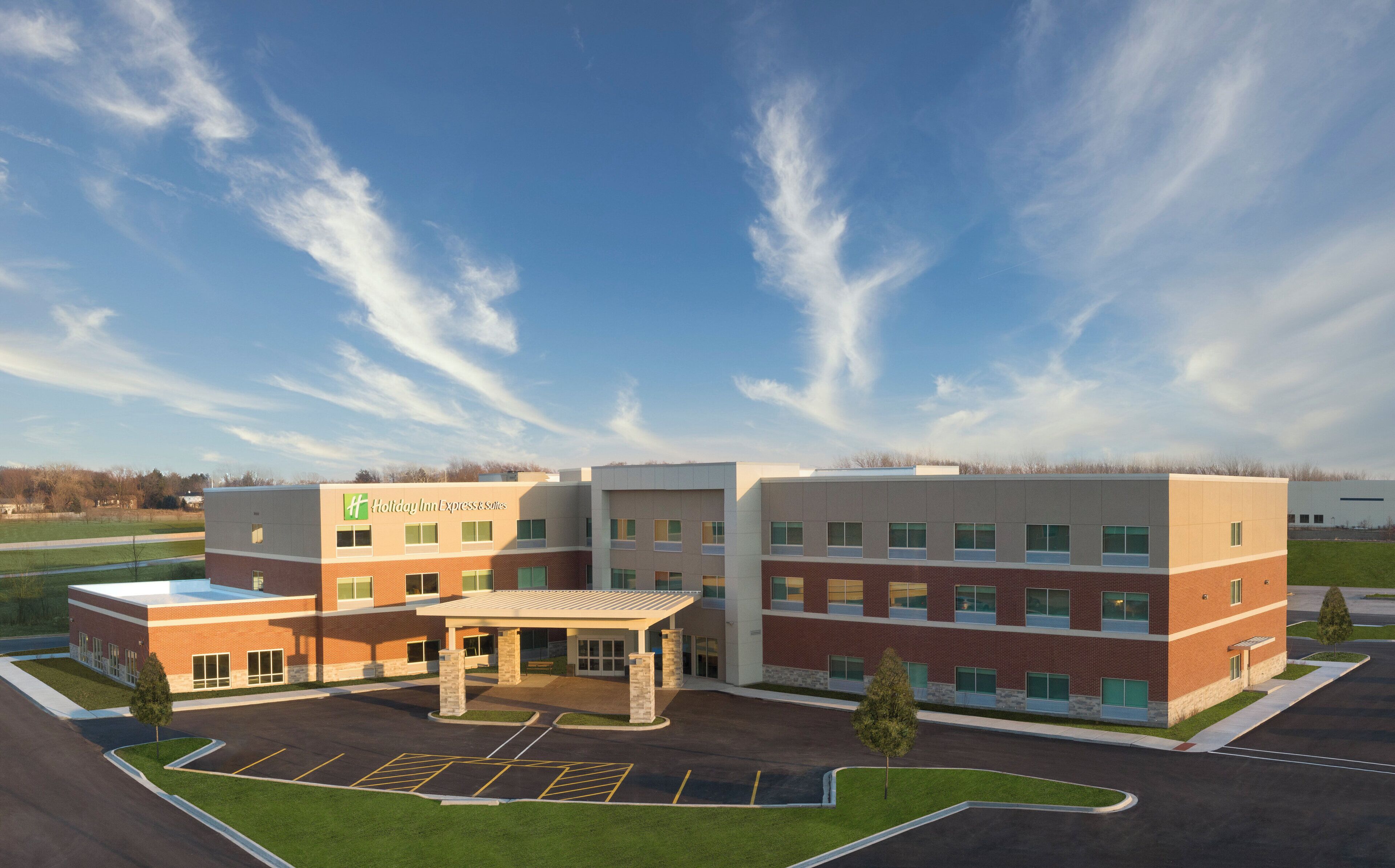 A Holiday Inn Express & Suites hotel with a covered entrance, parking lot, and a clear sky.