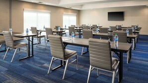 A conference room with tables and chairs, water bottles, and a flat-screen TV on the wall.