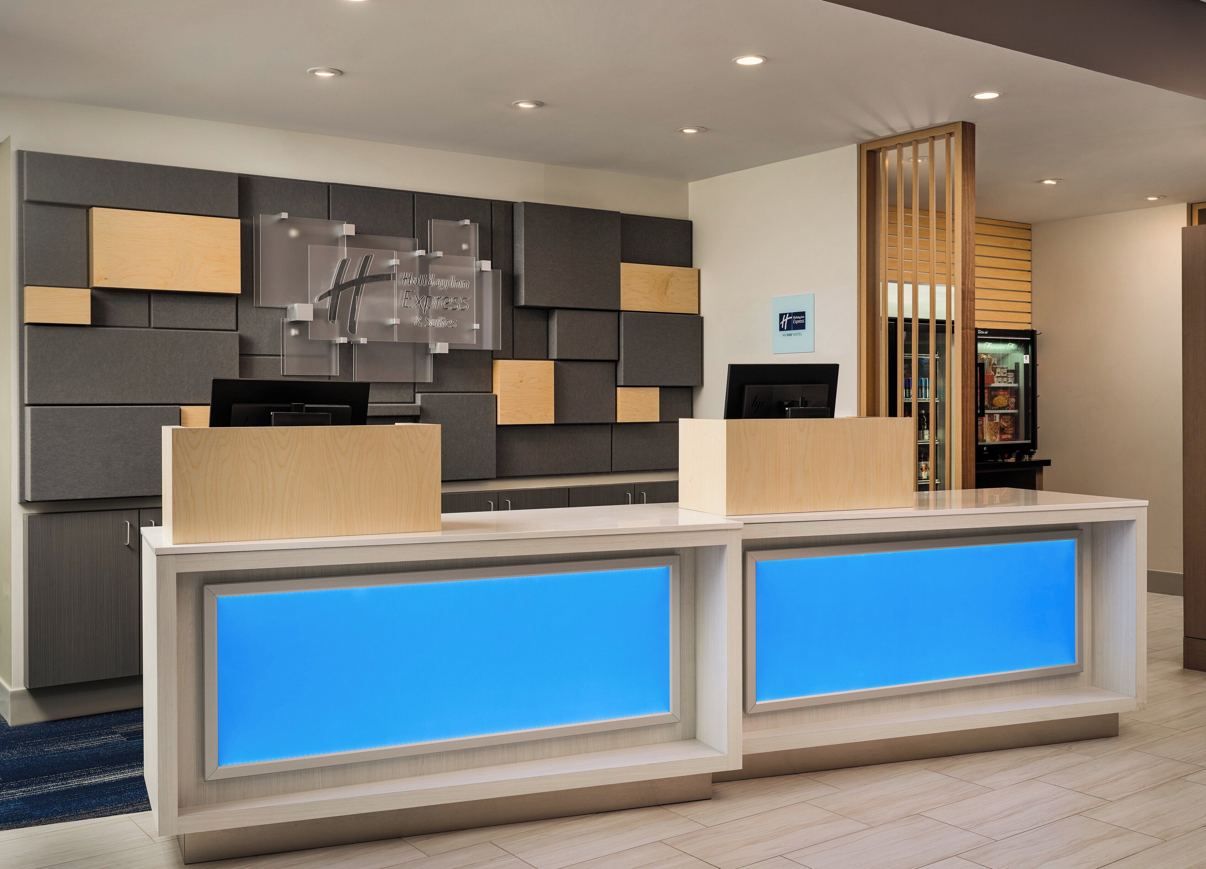 A modern hotel reception desk with a digital display, a refrigerator, and a wooden panel wall.