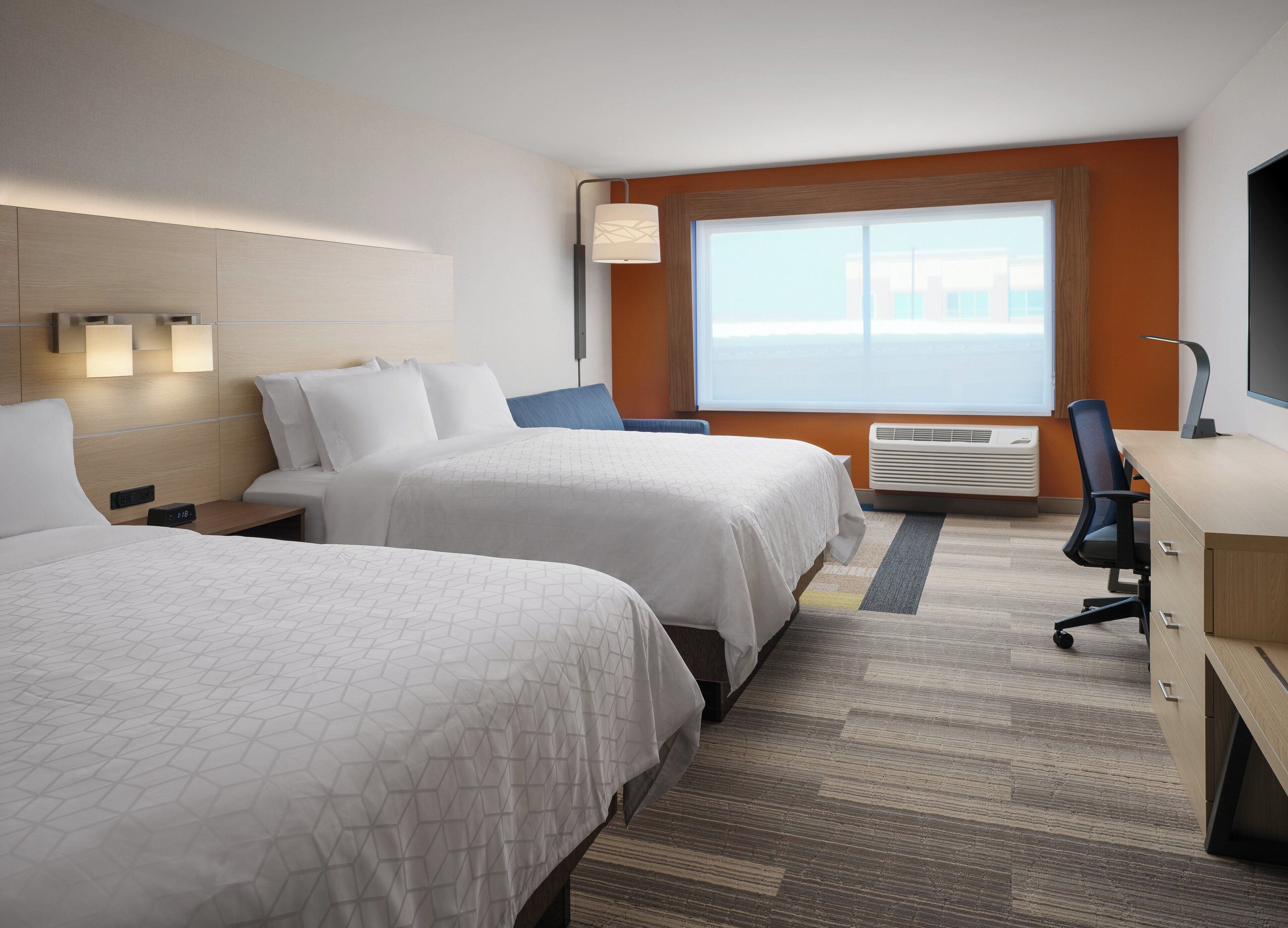 A hotel room with two beds, a desk, a chair, a lamp, and a large window.