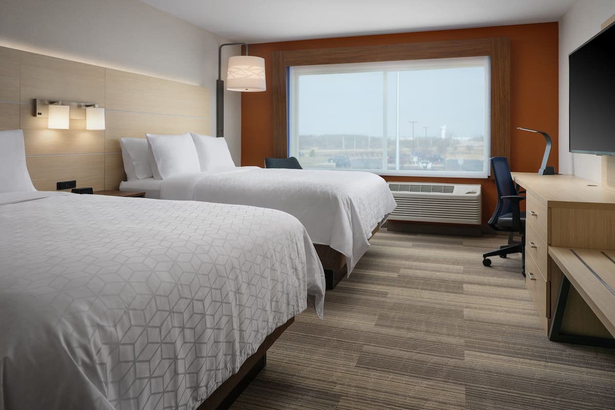 A hotel room with two beds, a desk, a chair, a TV, and a large window with a view.