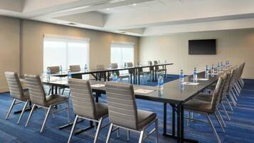 A conference room with a long table, chairs, water bottles, and a flat-screen TV on the wall.