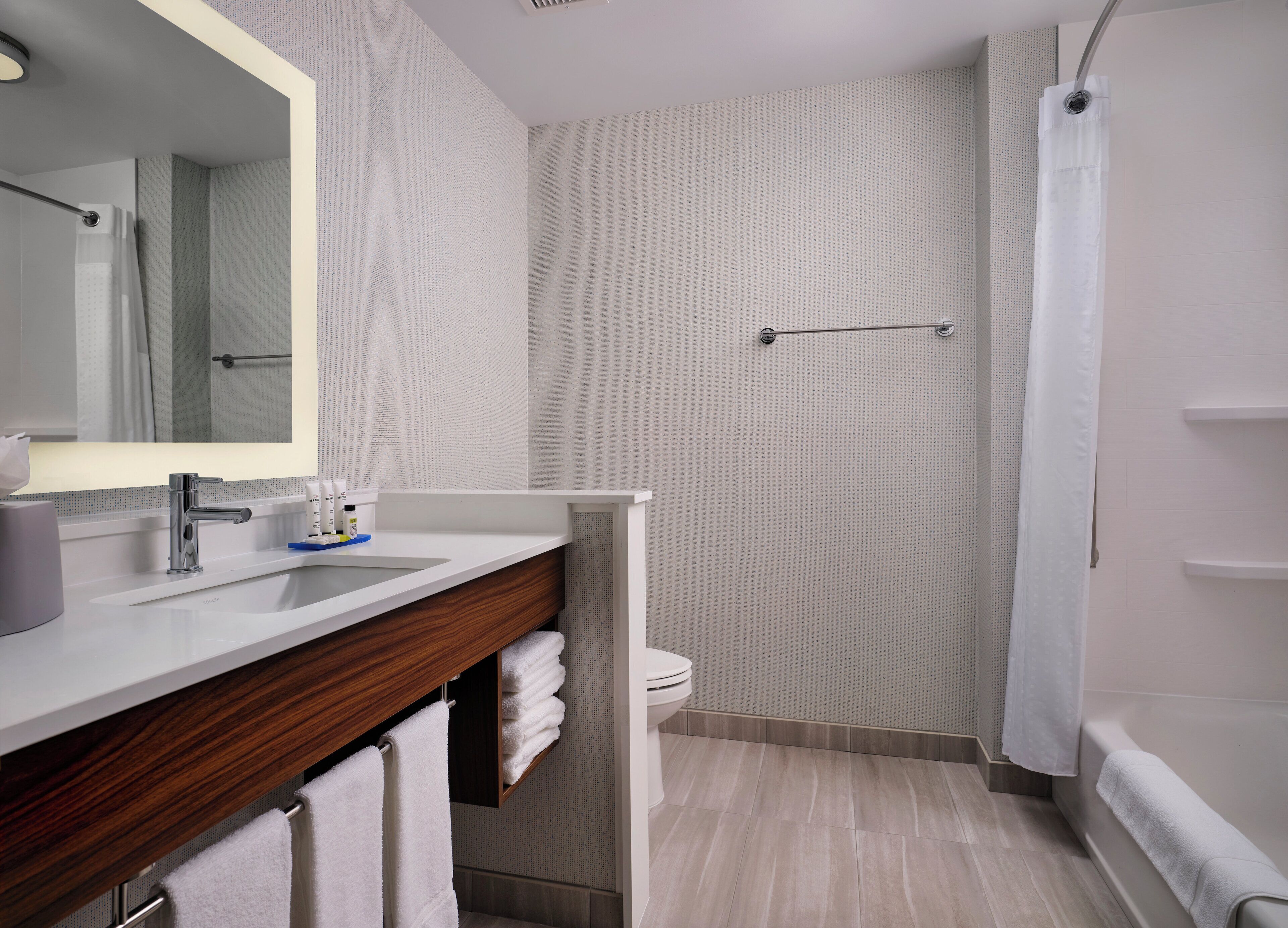 A modern bathroom with a wooden vanity, a large mirror, a toilet, and a shower area.