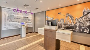 Zona de recepción de un hotel con un quiosco de check-in digital, una pared con citas de viajes inspiradoras y un mural de un paisaje urbano.