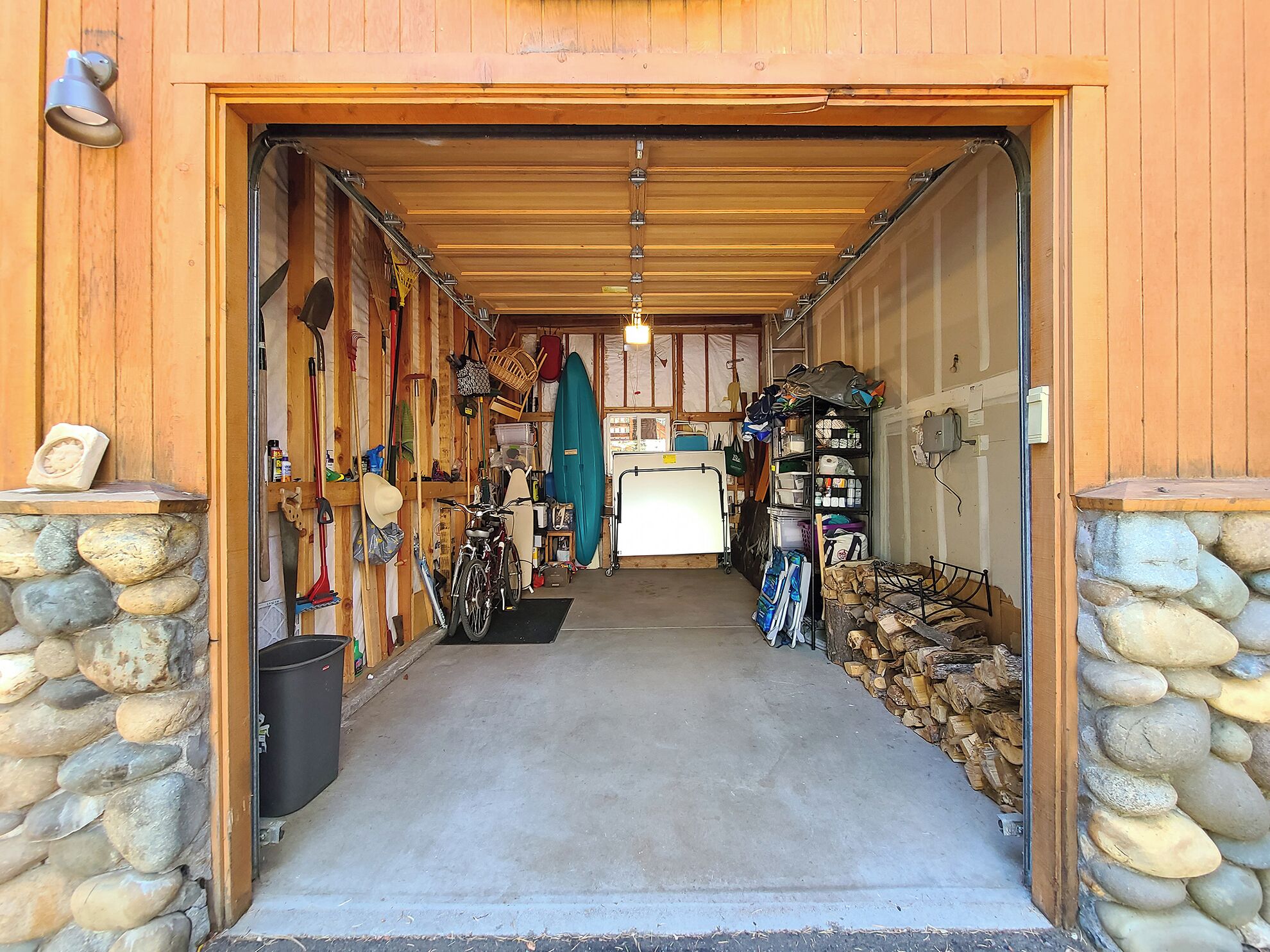 A garage with a concrete floor, wooden walls, and a stone wall on one side.