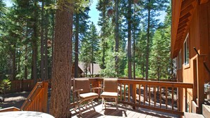 A wooden deck with chairs and a table, surrounded by tall trees. - Rosemor - 3 bedroom, 2 bath, fenced in back yard! Walk to Lake! (Tahoe City)