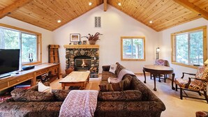 A cozy living room with a stone fireplace, wooden ceiling beams, and large windows offering views of the outdoors. - Rosemor - 3 bedroom, 2 bath, fenced in back yard! Walk to Lake! (Tahoe City)