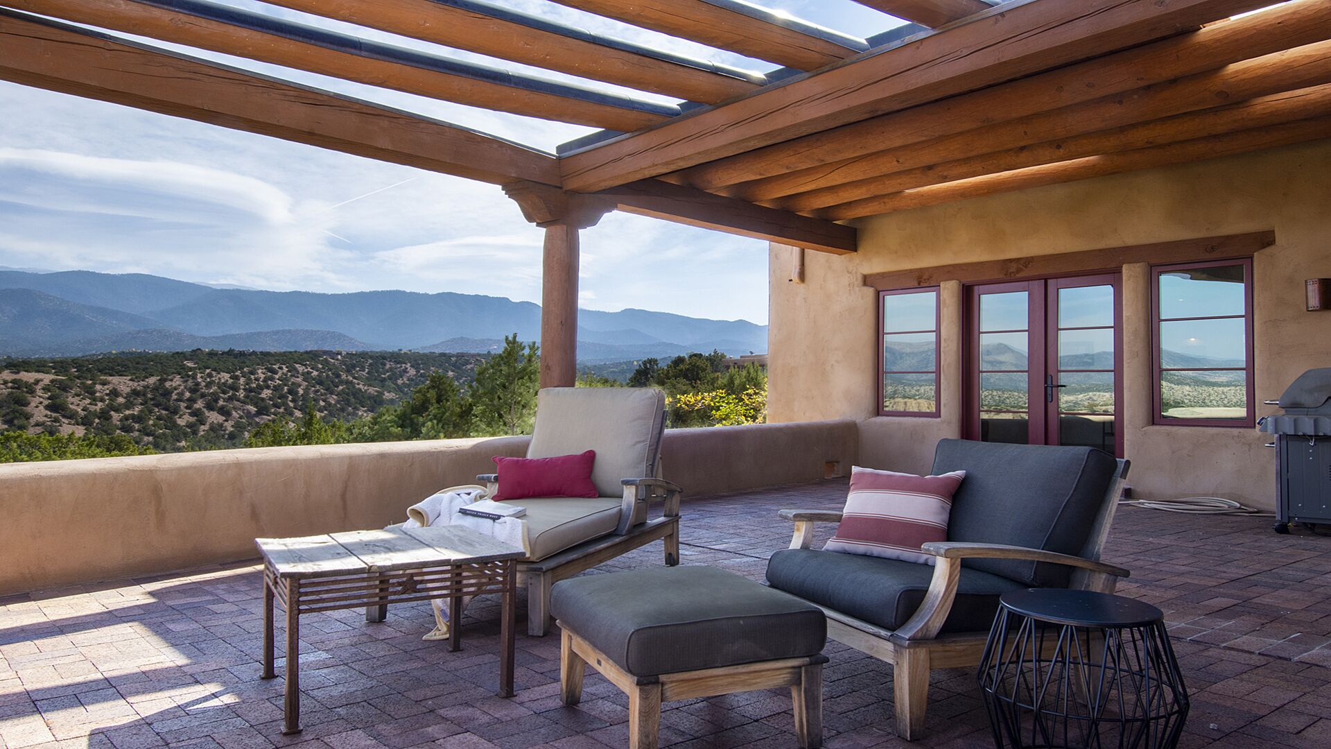 Un espace extérieur abrité avec des sièges, offrant une vue sur les montagnes, ainsi qu’un barbecue et une table de patio.