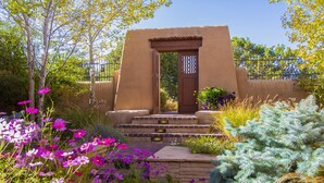 A traditional adobe structure with a wooden door, surrounded by vibrant flowers and greenery. - Elegant 3 bedroom home with stunning views and 5 star reviews! (Santa Fe)