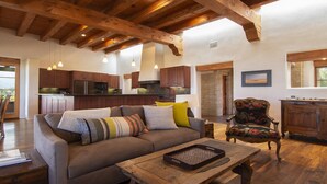 A spacious living area with a wooden ceiling, a sofa with colorful cushions, a wooden coffee table, and a rustic chair. - Elegant 3 bedroom home with stunning views and 5 star reviews! (Santa Fe)