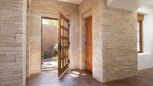 A hallway with stone walls and wooden doors, leading to an outdoor area with plants. - Elegant 3 bedroom home with stunning views and 5 star reviews! (Santa Fe)