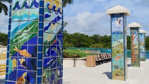 Une structure recouverte de carreaux de céramique, ornée de fresques représentant la vie marine, sous un ciel dégagé, et bordée d’une zone pavée.