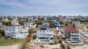 Ett bostadsområde vid kusten med flera tvåvåningshus, en swimmingpool och en strand i bakgrunden.