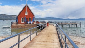 A wooden pier leading to a red building with a triangular roof, a sandy beach, and a calm lake with boats. - Chambers Delight House - Chambers beach & pool & tennis * 4 bedroom, 2.5 bath (Tahoma)
