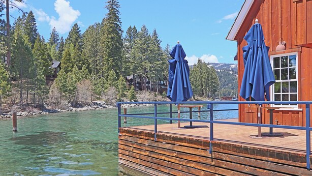 A wooden dock extending into a clear lake, with a building featuring large windows and blue umbrellas. - Chambers Delight House - Chambers beach & pool & tennis * 4 bedroom, 2.5 bath (Tahoma)