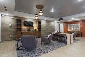 A modern dining area with a wooden table and chairs, a flat-screen TV mounted on the wall, and pendant lighting. - Candlewood Suites San Antonio - Schertz (Schertz)