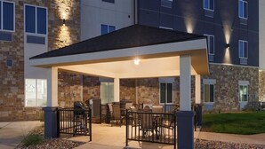 A covered outdoor patio with seating and a grill, surrounded by a stone building with multiple windows and a stone facade.