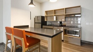 A modern kitchen with a central island, built-in wooden shelves, stainless steel appliances, and pendant lighting.