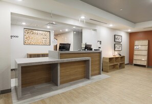 A reception desk with a wooden finish, a white wall with a geometric pattern, and a wooden floor. - Candlewood Suites San Antonio - Schertz (Schertz)