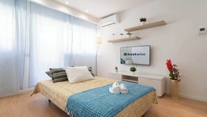 Ein modernes Hotelzimmer mit einem Bett, einem Schreibtisch, einem Sessel, einem Fernseher und einer Pflanze.