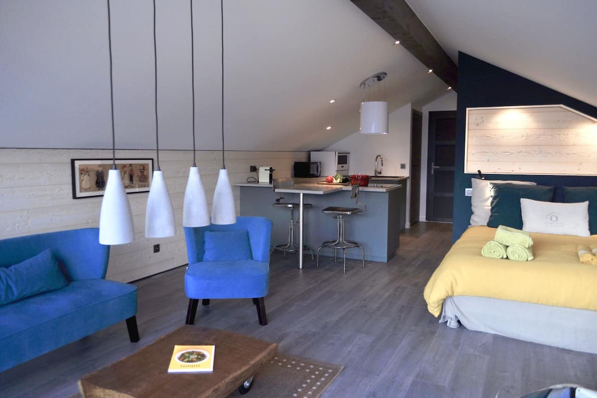 Un salon moderne avec un canapé bleu, une table basse et un lit recouvert d’une couverture jaune.