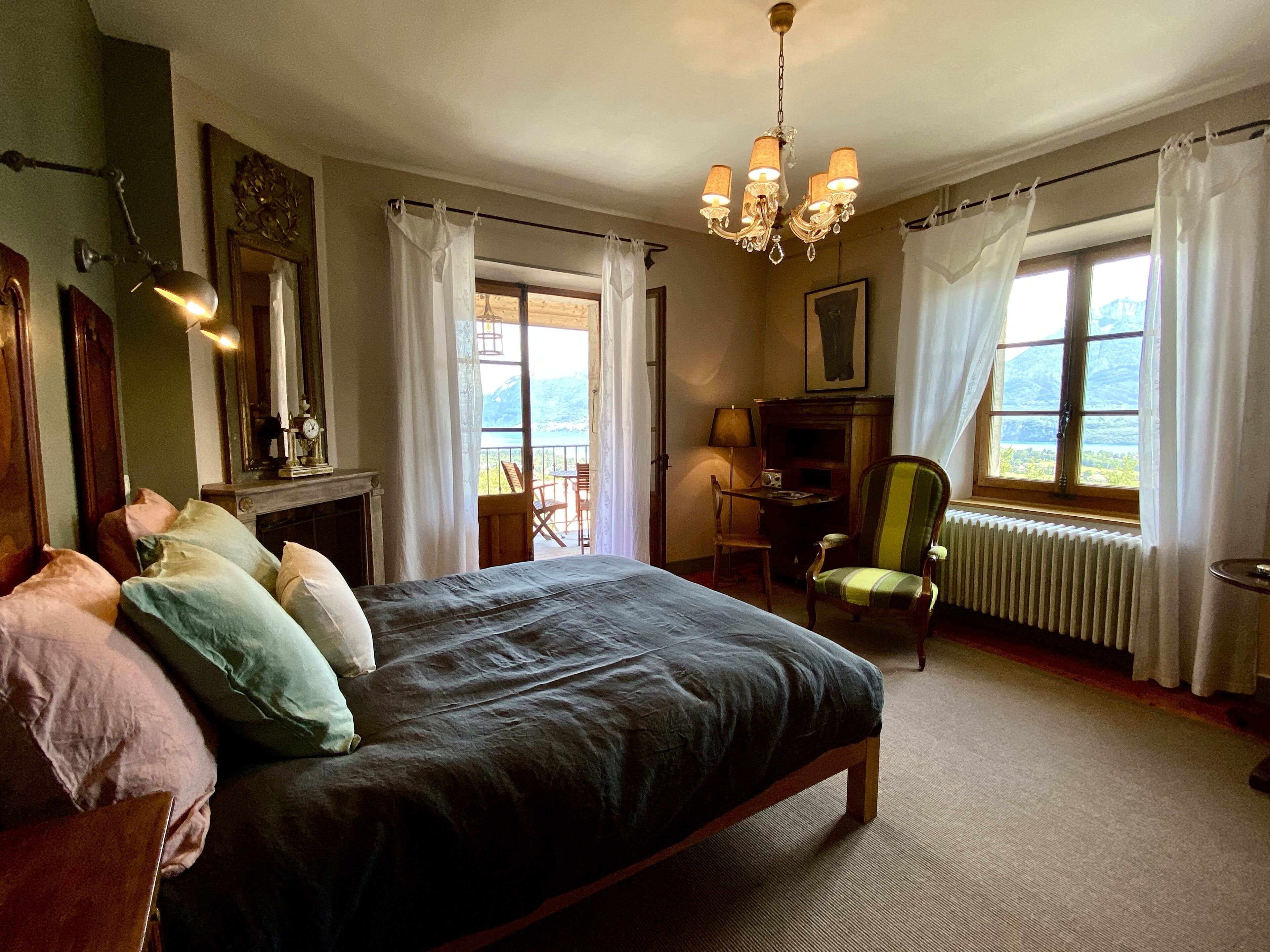 Une chambre avec un grand lit, un bureau, une chaise, un radiateur et une vue sur l’extérieur.