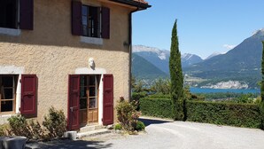 Une maison avec un toit recouvert de tuiles rouges, une façade en pierre et une vue sur les montagnes et un lac.