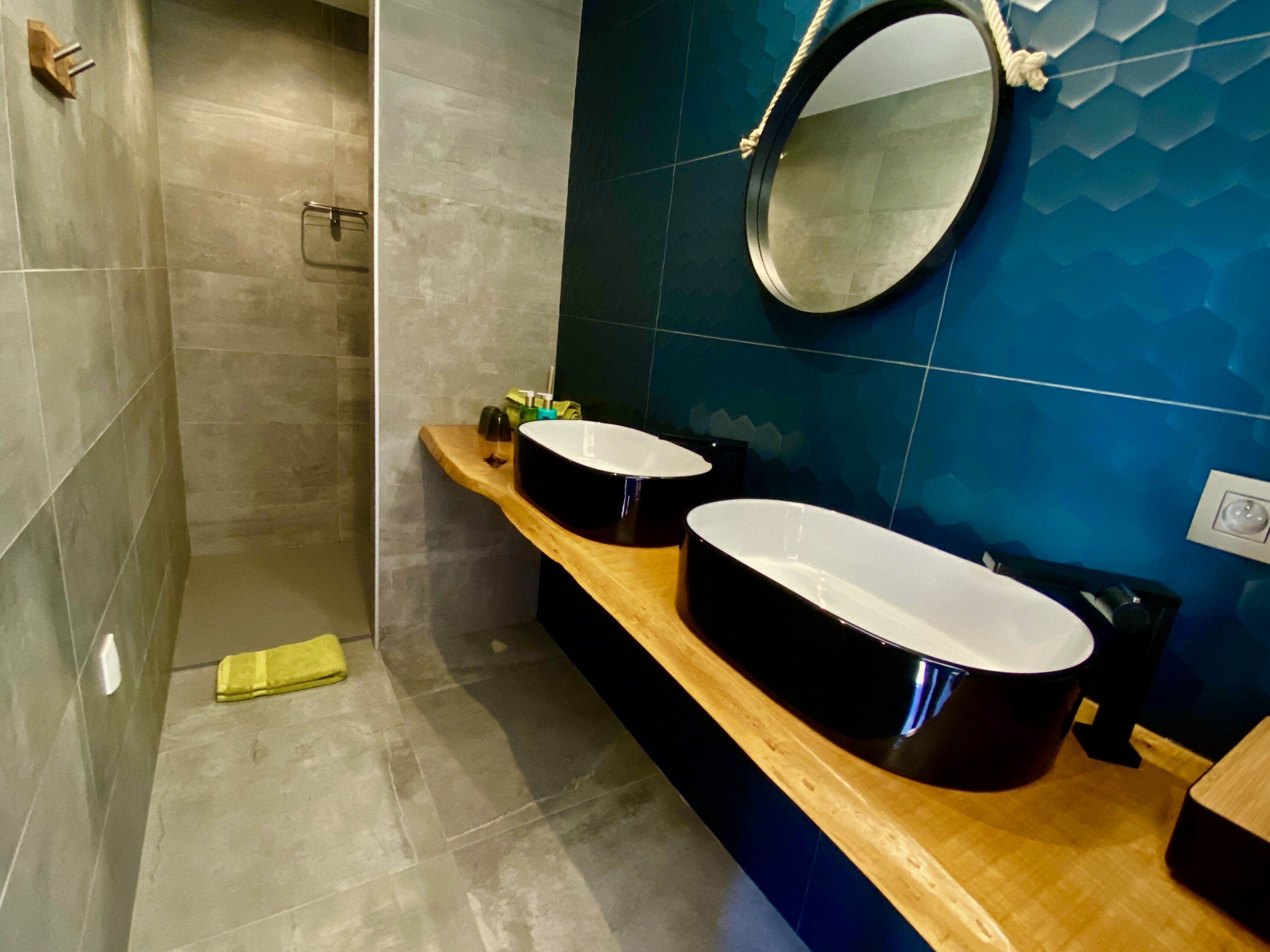 Un baño moderno con dos lavamanos, un mueble de tocador de madera, un espejo y zona de ducha.