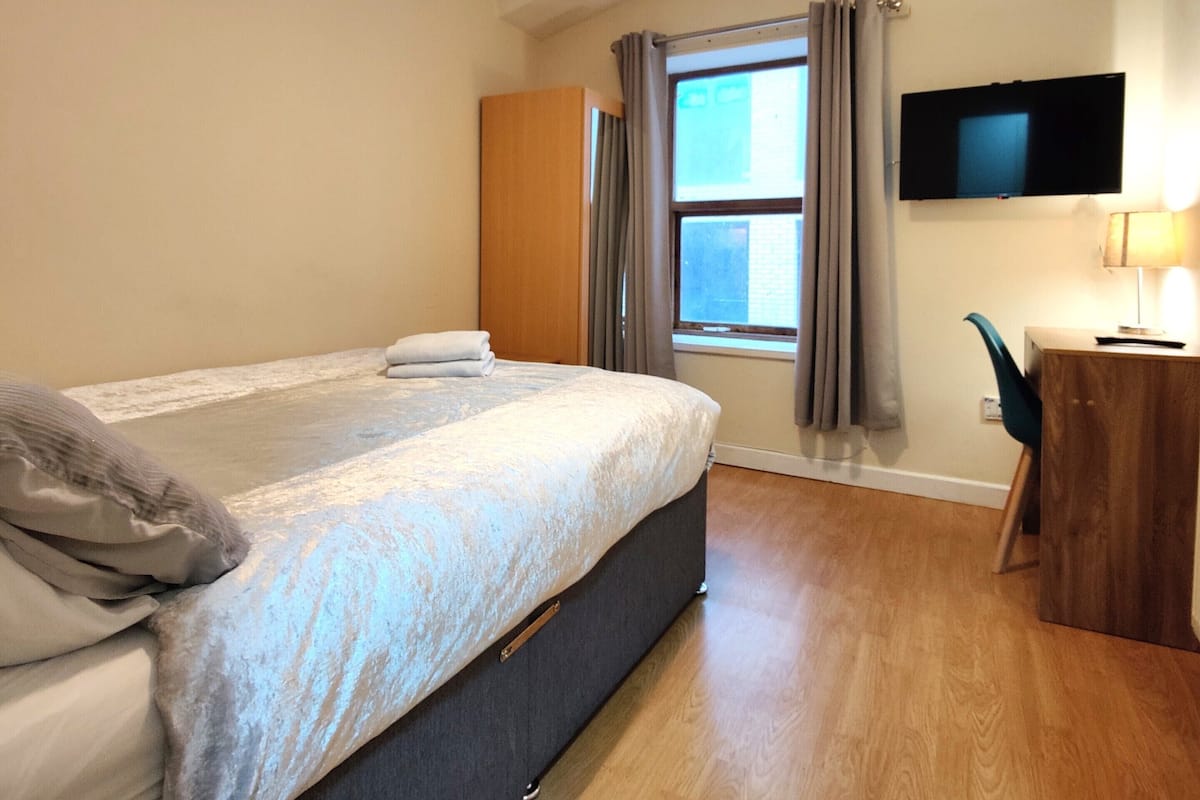 Une chambre d’hôtel équipée d’un lit, d’un bureau, d’une chaise, d’une télévision et d’une fenêtre avec des rideaux.
