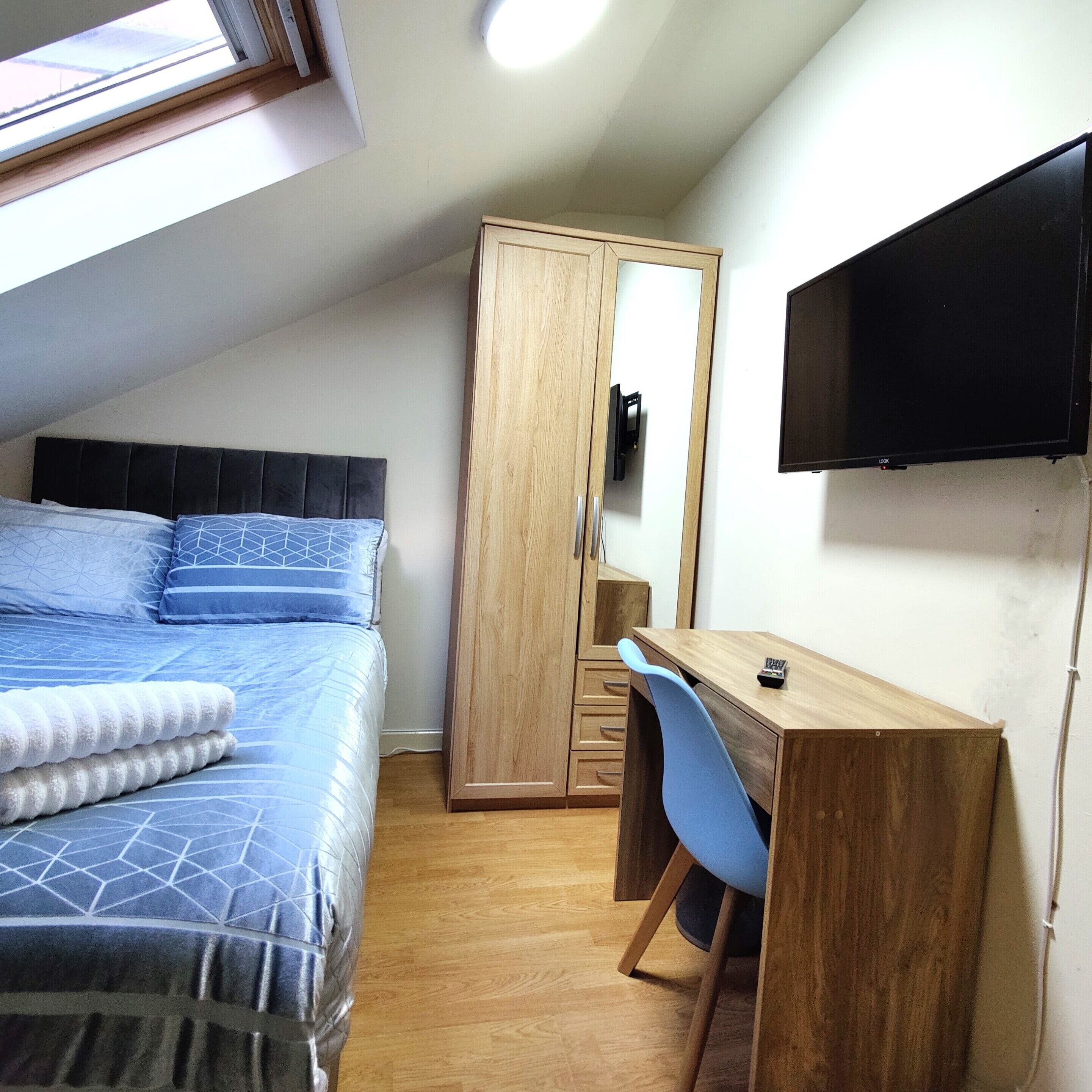 Un dormitorio con cama, escritorio, silla, armario y televisor montado en la pared.