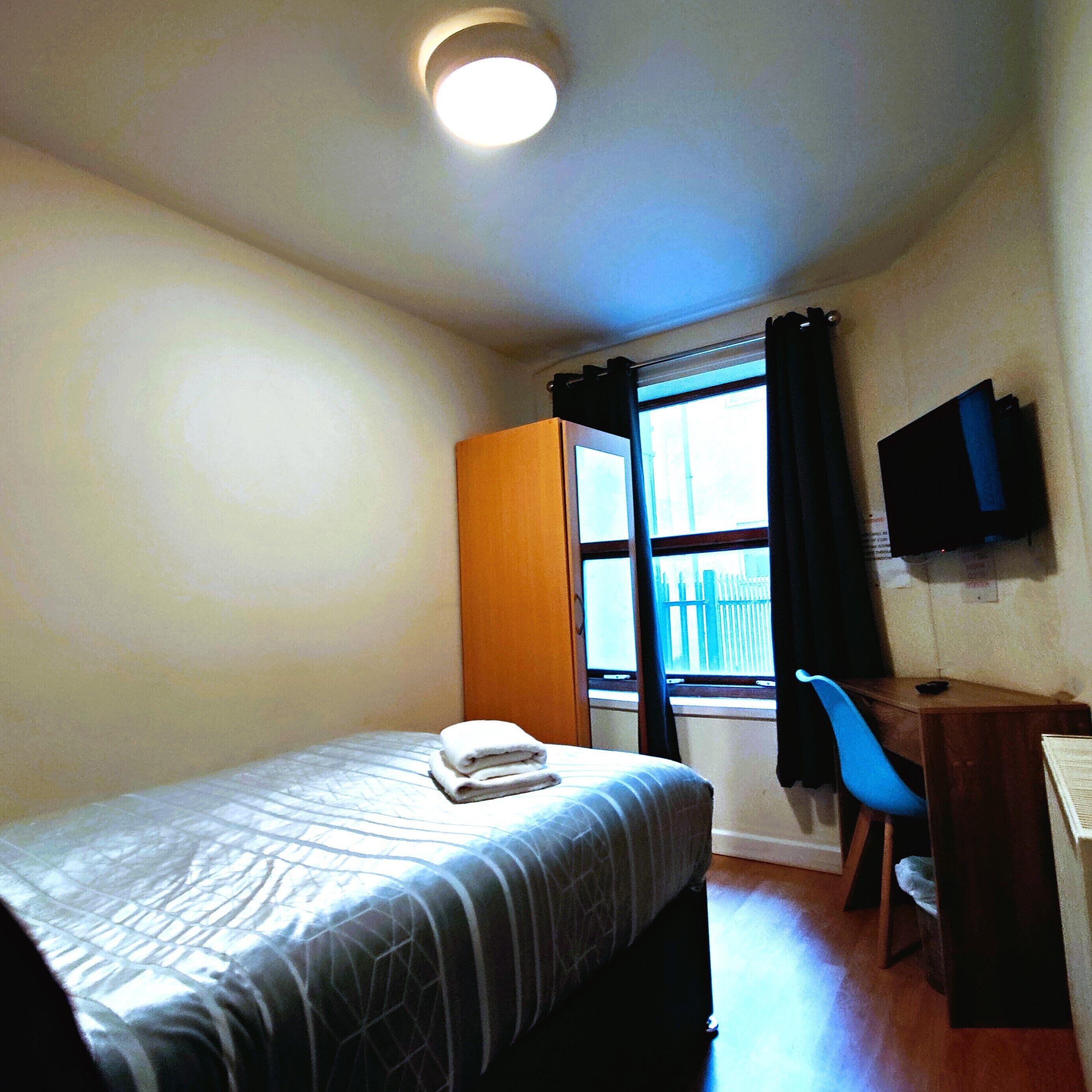A hotel room with a bed, a desk, a chair, a television, and a window with curtains.