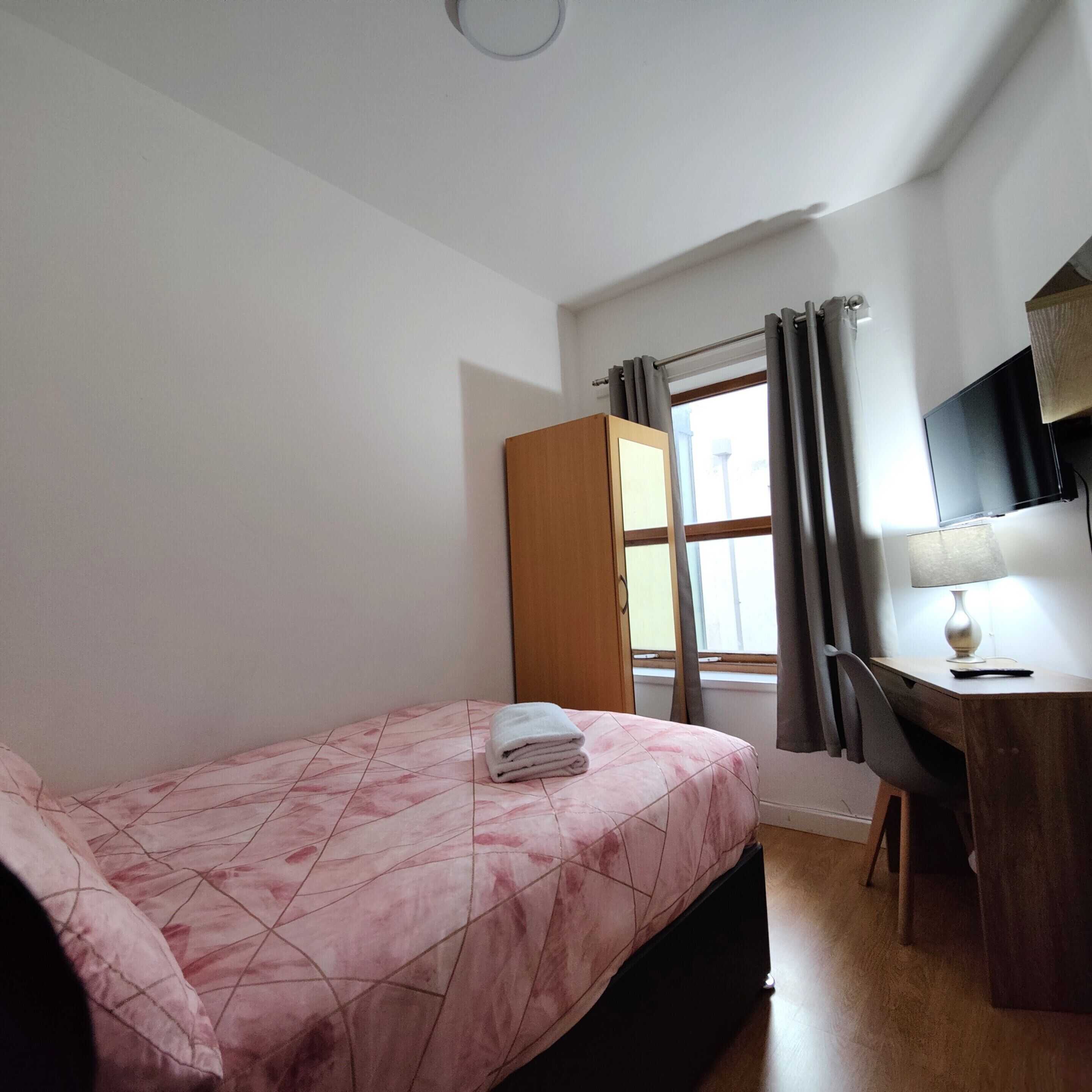 Une chambre à coucher avec un lit, un bureau, une télévision et une fenêtre avec des rideaux.