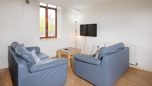 A living room with two blue sofas, a small wooden table, a floor lamp, and a TV mounted on the wall. - Liverpool Stays - City Centre Rooms (Liverpool)