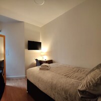 A hotel room with a bed, a desk with a chair, a flat-screen TV mounted on the wall, and a lamp.