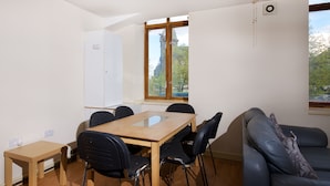 A room with a wooden table, black chairs, a small side table, a couch, and a window with a view of trees and a building. - Liverpool Stays - City Centre Rooms (Liverpool)